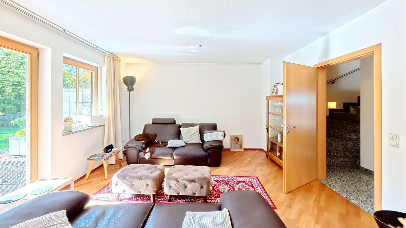 Startansicht eines 360°-Immobilienrundgangs: Wohnzimmer einer Doppelhaushälfte mit Ledersofas, Parkett, Fenstern zum Garten und offener Tür zum Treppenhaus