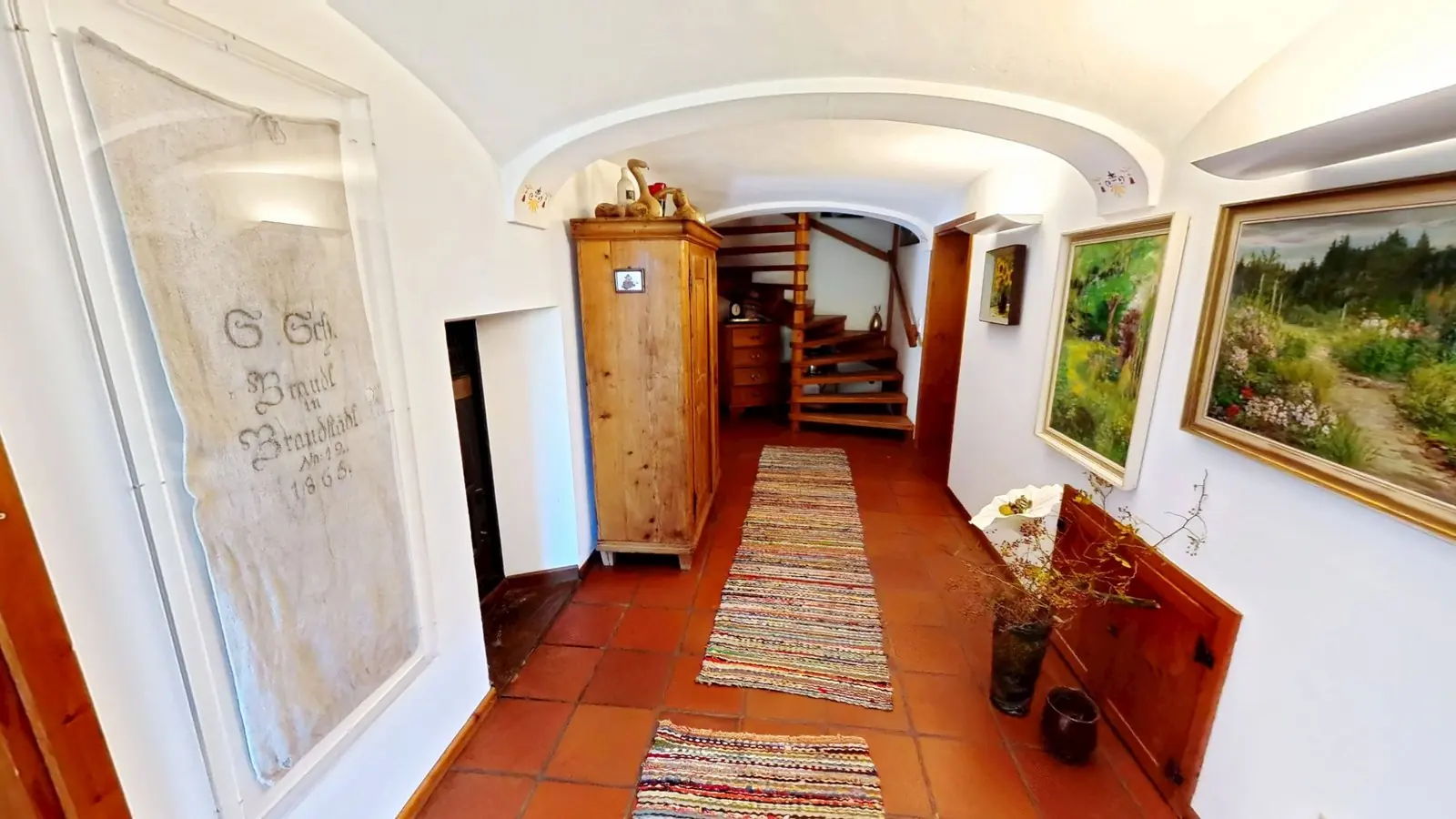 Startansicht eines 360°-Immobilienrundgangs: Flur mit Gewölbedecke, Terrakottaboden, Bauernschrank und Holztreppe