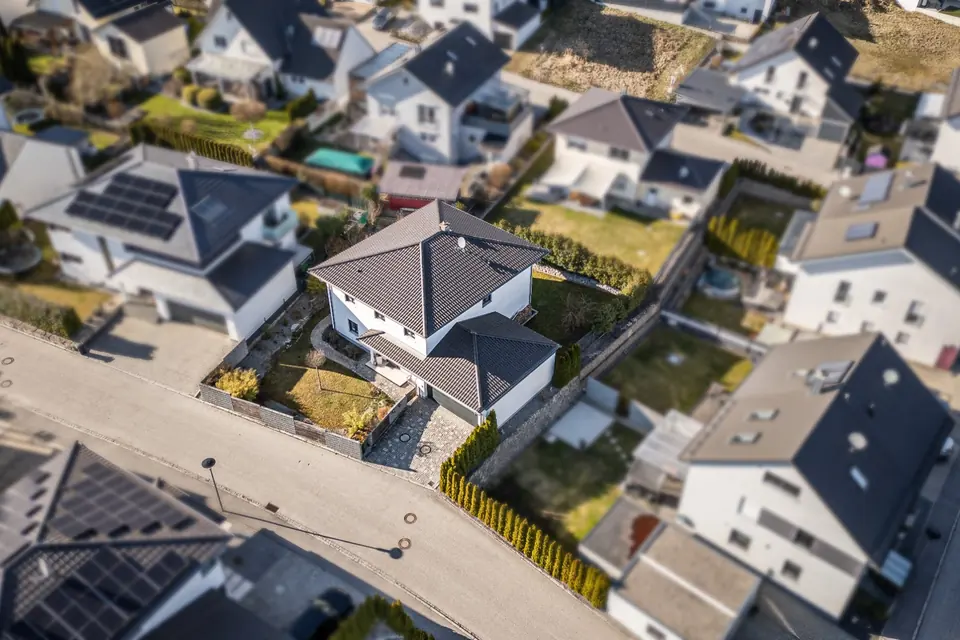 Drohnenaufnahme eines Einfamilienhauses mit Walmdach, Garten und Zufahrt in einem Wohngebiet
