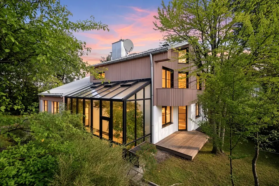 Einfamilienhaus mit Holzfassade, Wintergarten und Holzterrasse im Abendlicht zwischen Bäumen