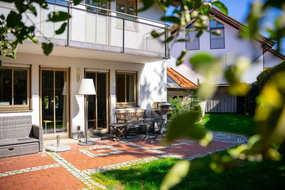 Gepflasterte Terrasse mit Gartenmöbeln vor einem Haus mit Balkon im Sommerlicht