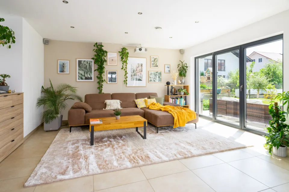 Helles Wohnzimmer mit Ecksofa, Bilderwand, Pflanzen und bodentiefer Terrassentür
