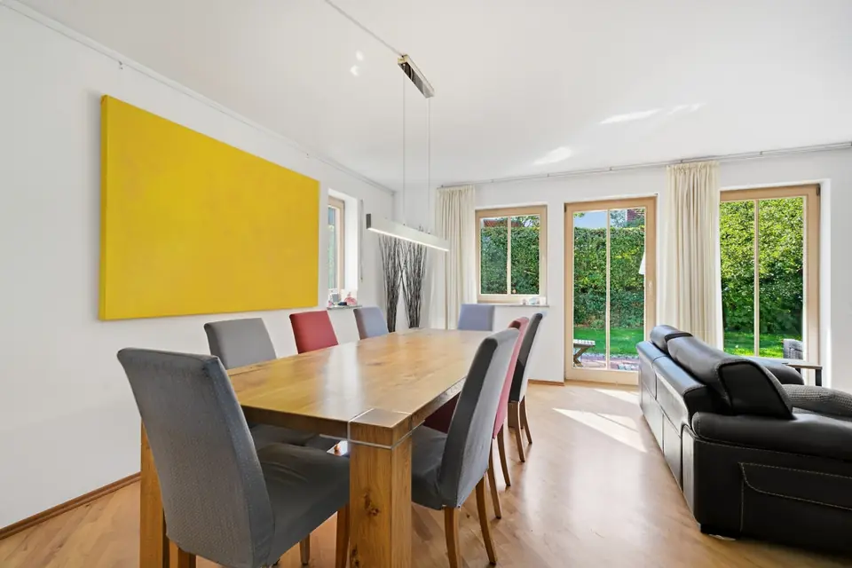 Essbereich mit Holztisch, farbigen Stühlen, gelbem Wandbild und Terrassentür