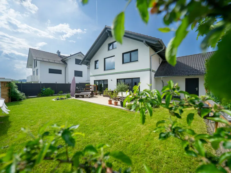 Einfamilienhaus mit Rasenfläche und Terrasse, durch Zweige hindurch fotografiert