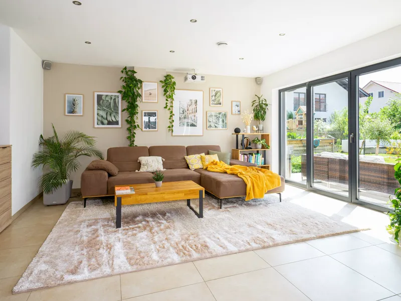 Helles Wohnzimmer mit Ecksofa, Bilderwand und bodentiefen Fenstern zur Terrasse